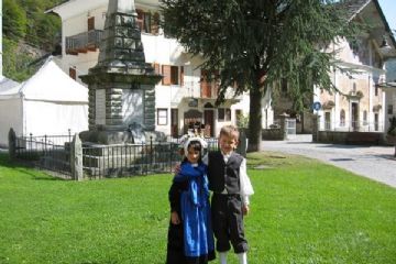 Una coppia di bambini issimesi con il costume tradizionale, con sullo sfondo il monumento ai Caduti